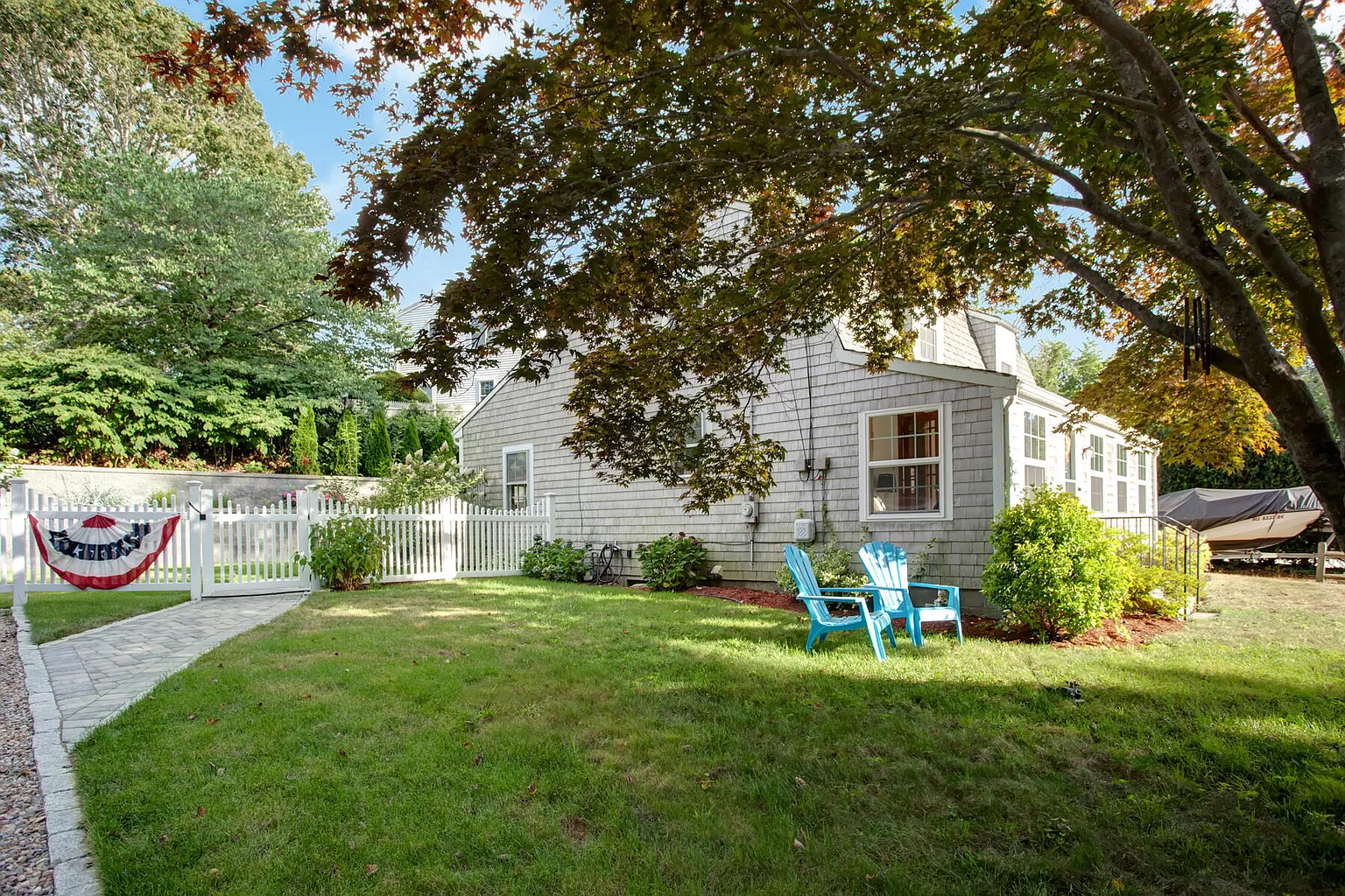 Backyard with picket fence and Adirondack chairs under a maple tree.