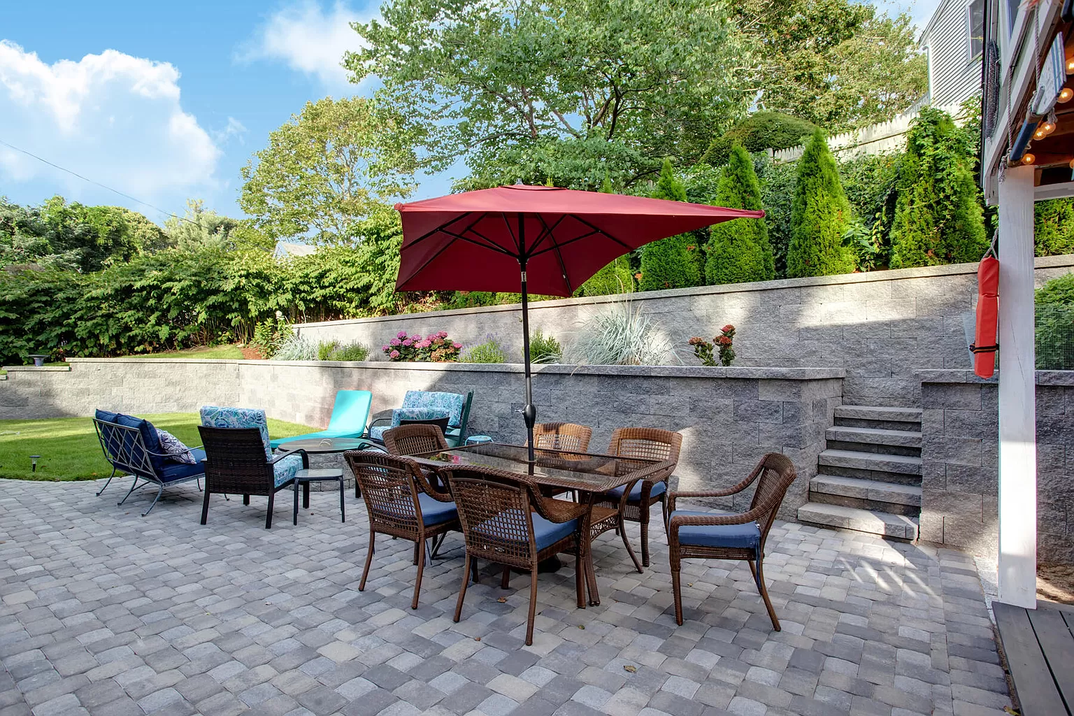 Patio dining set with red umbrella and lounge chairs.